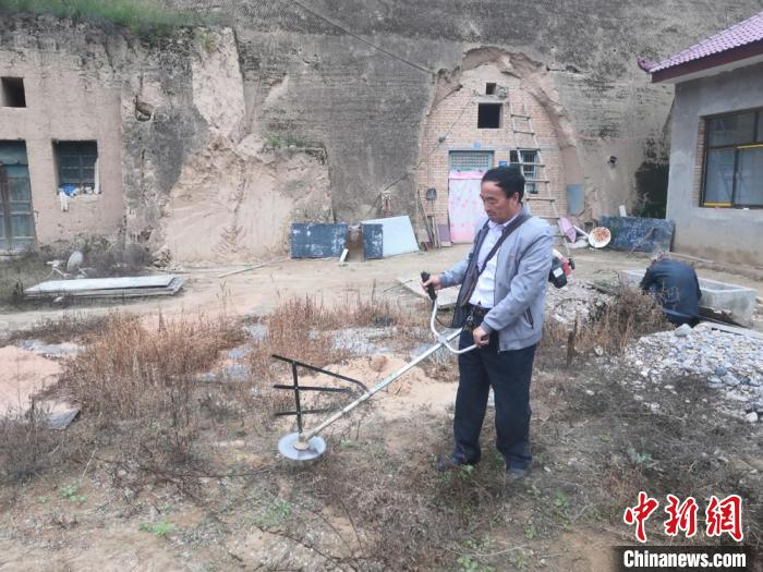 图为胡建国帮助贫困户清理院落杂草。(资料图) 杨康 摄