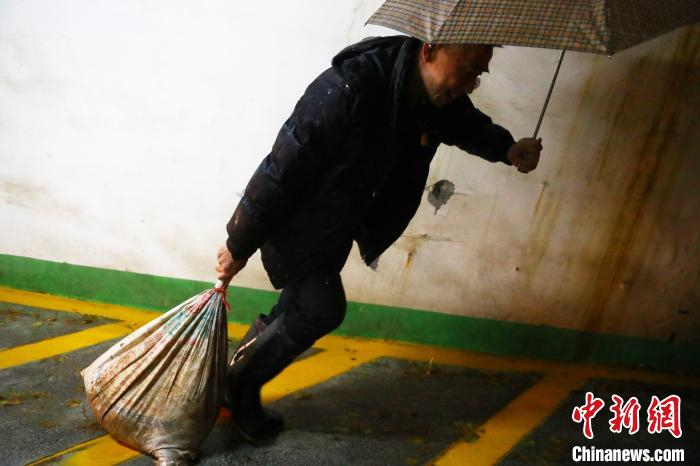 图为社区工作人员正提着沙袋去封堵灌入车库的积水。　刘占昆 摄