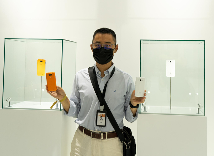 一位米粉拿着自己购买的小米1和小米2手机与柜台里的展示机合影（许诺 摄）