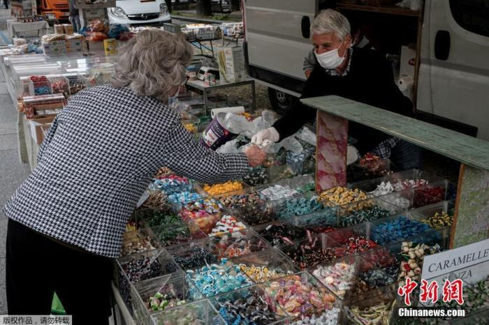 资料图：当地时间5月5日，曾经被列为意大利疫情“红区”的北部小镇圣菲奥拉诺逐步解封，一位民众正在糖果摊购物，这是该市场从2月21日关闭后首次开放。