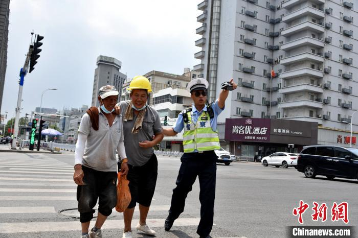 烈日下，交警搀扶受伤民工过马路。　朱志庚 摄