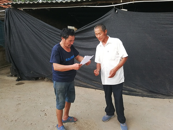 龙泉乡残疾人专职委员李举（右）把刚刚办好的残疾人证和享受政策清单送到李根手上