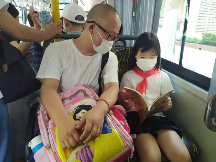 开学在即，小朋友们陆续返校领取新课本，图为49路公交车上，一名家长和孩子在翻阅刚领的新课本教材