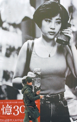 2008年，纪念改革开放30周年全国摄影大展在王府井步行街举办。一位行人手持小巧的手机，从一幅女青年持“大哥大”的巨型图片展板前经过。胡庆明/摄