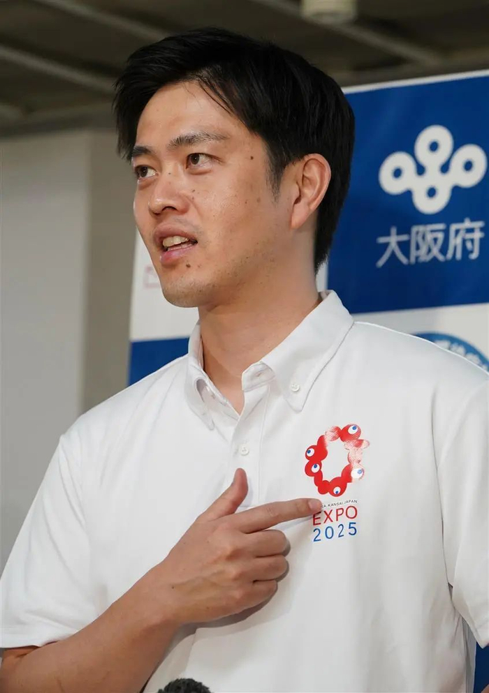 △ 吉村洋文穿着带有“光辉君”的宣传衫。8 月 26 日，吉村洋文面对媒体记者们表示：“真希望能快点穿上织好 logo 的衬衫！”图片来源 | 产经新闻