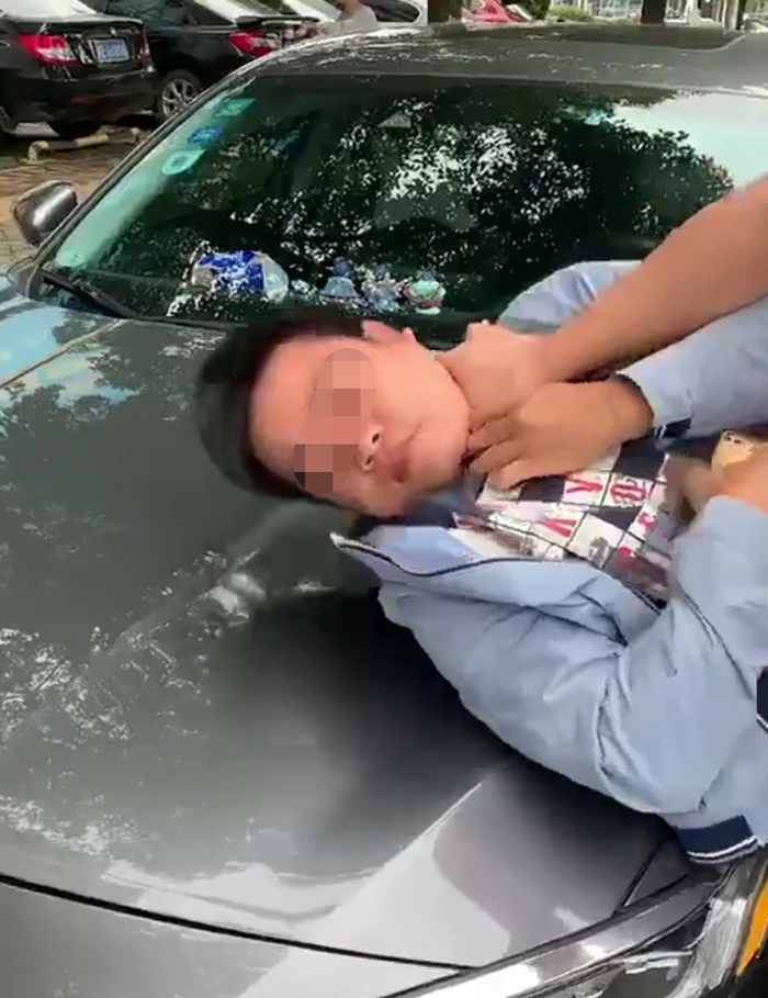网友发布的视频显示，疑似拍摄违停的男子被车主按在了前引擎盖上。视频截图