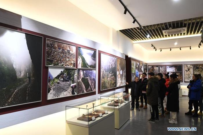 Mao Xianglin (1st, L) introduces the story of building roads in Xiazhuang Village to the audience at an exhibition hall at Xiazhuang Village, Zhuxian Township, Wushan County of southwest China's Chongqing, Jan. 6, 2021. For those who lived in Xiazhuang Village, it once took them two days to reach the nearest county. Thanks to the unceasing efforts of Mao Xianglin, the onerous travelling has become a history. In 1997, 38-year-old Mao Xianglin, the secretary of Communist Party of China (CPC) branch of Xiazhuang Village and head of the village committee, mobilized the villagers to build a better road to the outside world. To speed up the road building, Mao once worked and lived at the construction site for three months without going home. Finally in 2004, an 8-kilometer long and 2-meter wide road was finished. After more widening and hardening work conducted by the local government, the travel time from Xiazhuang Village to the county seat has been slashed to about one and a half hours. For Mao, building a road is the first step, and seeking a way to prosperity is the second. After consulting experts, he decided to develop orange planting industry in the village. Now, the orange orchard here covers an area of about 650 mu (about 43.3 hectares), and the whole village has shaken off poverty in 2015. 