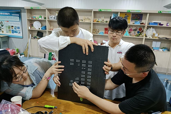 冯伯尧（左二）、孟书绮（左一）与指导老师在进行盲文阅读器的调试（三十七中供图）