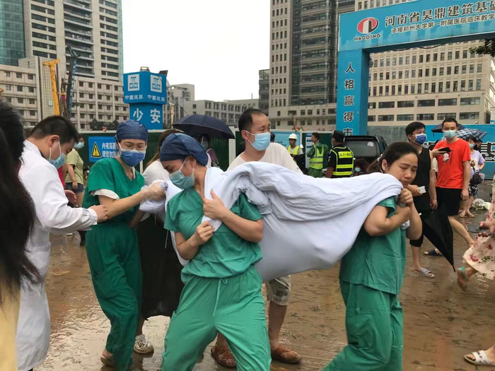 7月21日下午，郑大一附院（河医院区）安排患者转院，因担架不足，医院门前拥堵。医护人员用被褥做担架将患者抬走。 新京报记者 聂辉 摄