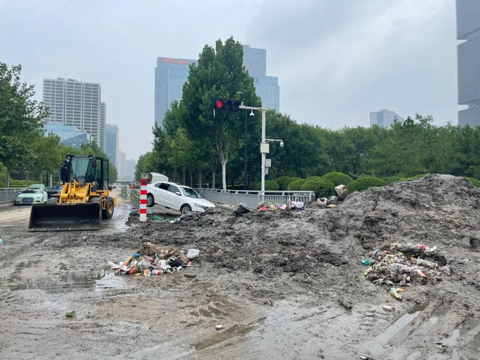 　　7月23日，事发地南边100米，郑州市普惠路与东站北街十字路口仍有大量淤泥，白色的轿车悬空在自行车道的护栏上。新京报记者 涂重航 摄