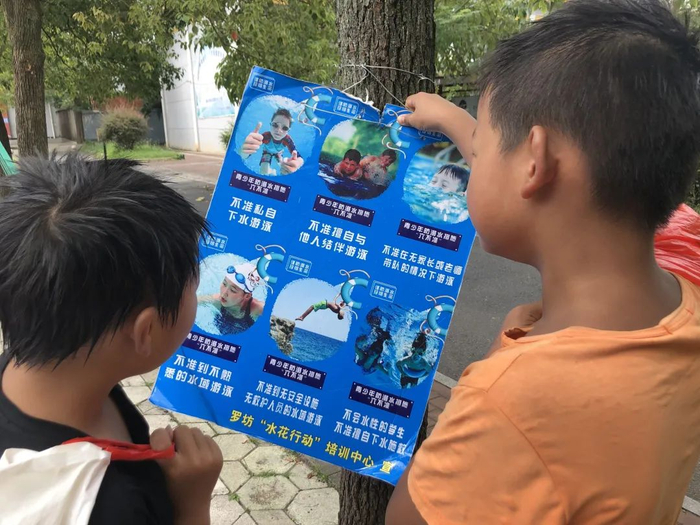 ▲7月27日，罗坊镇希望小学，结束游泳考试后，两个学生正在看防溺水教育宣传牌。新京报记者 杜寒三 摄