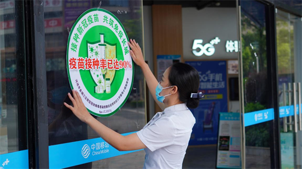在河池市金城江区，移动营业厅工作人员正在张贴由当地新冠肺炎疾控工作领导小组认证的“疫苗接种率已达90%”标识（央广网发 中国移动广西公司供图）