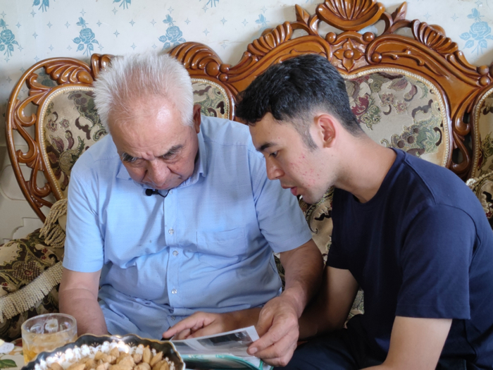 早上10点，吃完早饭，爷爷马合木提·买提热木又拿出老相册，给孙子阿地力江·阿卜杜力讲过去他做哈密瓜生意时的趣事。周杭 摄