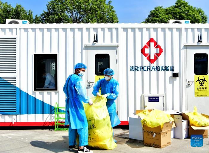 Staff members dispose medical waste outside a PCR (polymerase chain reaction) lab for nucleic acid testing in Xianyou County, southeast China's Fujian Province, Sept. 14, 2021. Three PCR labs have been built in the county to boost nucleic acid detection capacity. (Xinhua/Wei Peiquan)