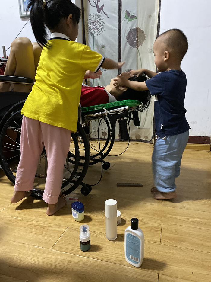  李小中的外孙（右）玩起过家家，给她化妆，李小中动不了，只是在轮椅上笑。