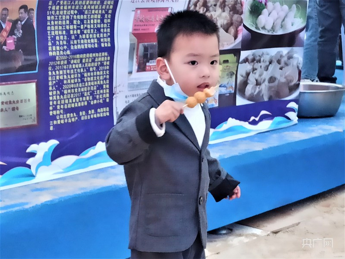 小男孩开心的吃着鱼丸，在鱼丸摊前流连忘返（央广网记者罗晓英 摄）
