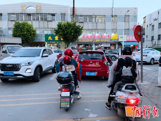 &nbsp;&nbsp;&nbsp;&nbsp;黄春花接放学的女儿回家（左），这条路上来接孩子的多数都是妈妈，她们要骑着电动车穿梭在汽车之间。中青报·中青网记者&nbsp;王景烁/摄