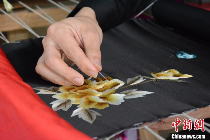 “绣郎”戴军正在绣制牡丹花图案的旗袍。　吕妍 摄