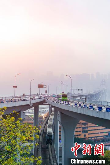 图为重庆菜园坝长江大桥下，轨道交通3号线列车与桥上桥下车流交错而行，远处是晨雾笼罩的重庆南岸区建筑。　陈鑫 摄