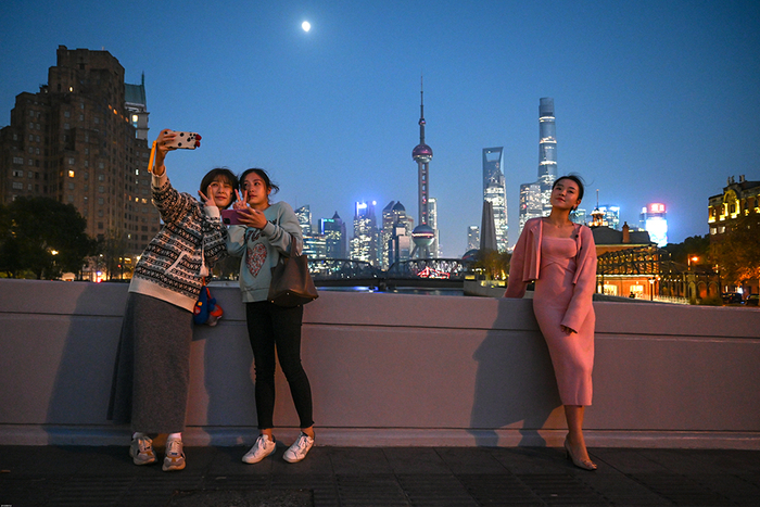 2021年11月16日，乍浦路桥，夜幕下，三位女生以陆家嘴为背景在各自拍照。