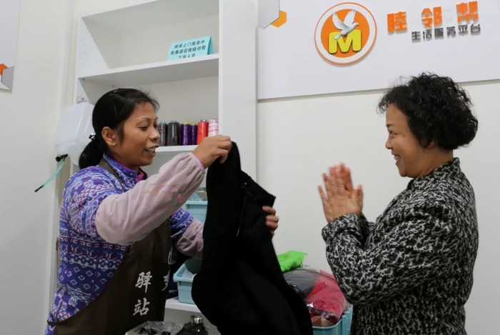 成都成华区二仙桥街道下涧槽社区党群服务中心的工作间，缝纫师傅张莉（左）向前来取件的居民展示为她缝好的衣服 谢秀栋 摄