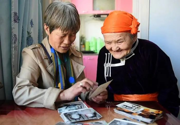 资料图：2017年5月10日，“草原母亲”都贵玛(右)和她抚养过的斯日巴勒在一起翻看照片。新华社记者 任军川 摄