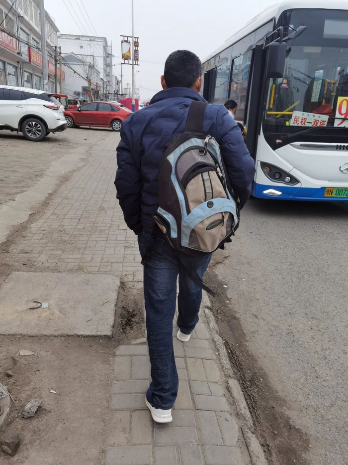 ▲吴春红走在街上，侄子上学时淘汰的双肩包背在肩上，背包外侧拉链坏了，口子敞开。新京报记者 苑苏文 摄