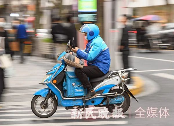 今天上午，南京西路泰兴路口，外卖骑手边开助动车边看手机。新民晚报记者 陶磊 摄