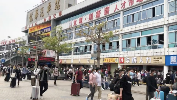 龙观人才市场前，拖着行李箱准备集体乘大巴前往厂区的求职者们。图/柳书琪