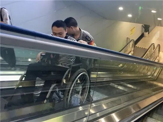 没有直梯，只能由人推轮椅乘扶梯的郭子成。受访者供图