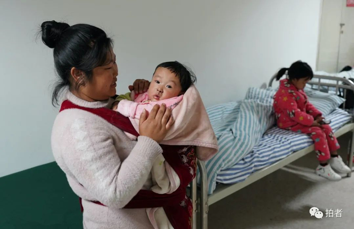 ▲罗进春的妻子怀里抱着术后的罗天昊，6岁的女儿罗昕秀坐在床上，她也是唇裂，于4月17日完成了唇裂手术。他们有3个孩子，2岁的儿子出生健康。