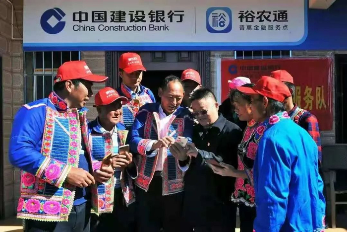 ▲彝族群众在建行员工指导下学习用“裕农通”APP办理政务