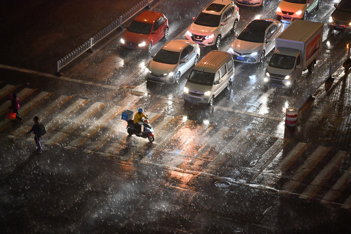 外卖骑手在风雨中骑行过马路。 新华社发（孙凡越 摄）