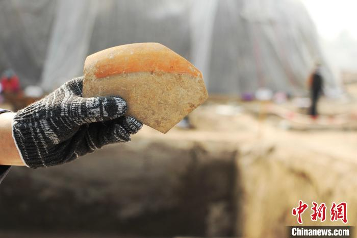 考古人员展示出土的红顶钵碎片。　赵晓 摄