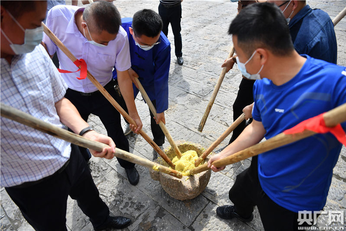 来往的游客们正在体验打米果（央广网记者 胡斐 摄）