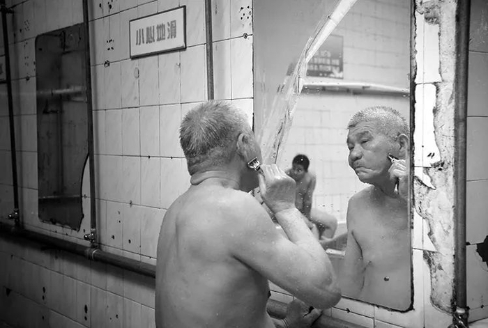 4月10日，一位老爷子泡完澡后对着镜子边冲头边刮胡子。