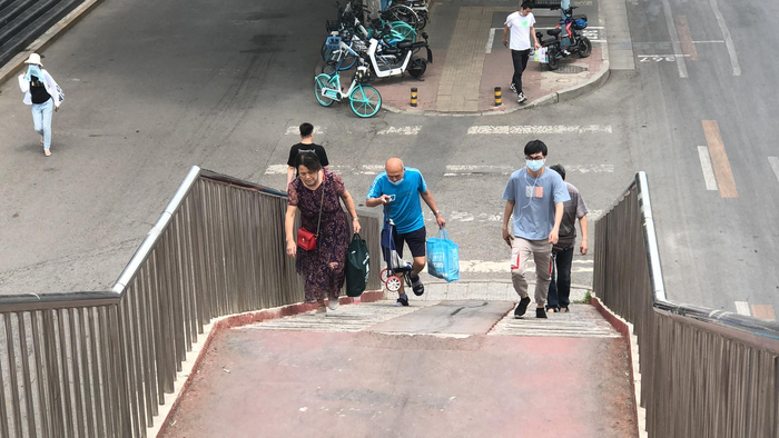 （提着菜篮、拎着菜车，老人艰难地爬上了没有电梯的过街天桥。）