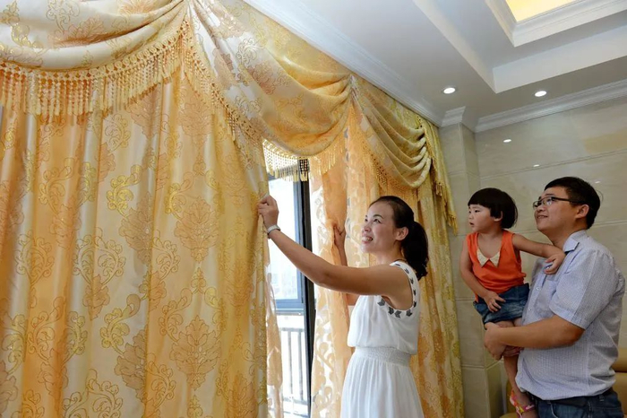 江西籍外来工毕红梅（左）和家人在晋江市内的新居里整理窗帘（张国俊/摄）