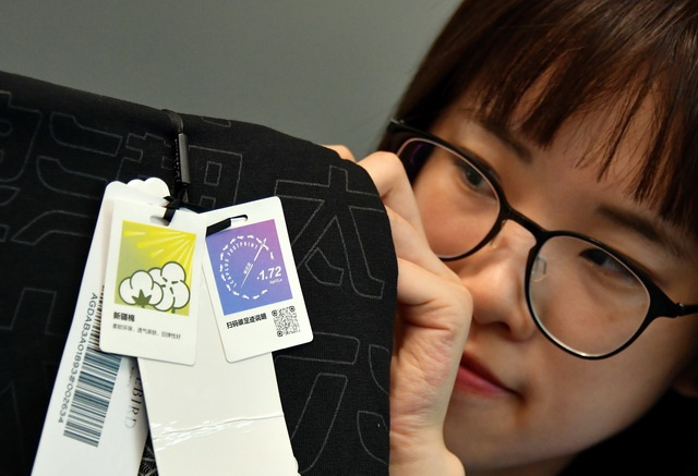 （6月1日，太平鸟时尚服饰一位工作人员向记者展示印有碳足迹内容的服装吊牌。摄影/章轲）