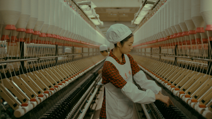 图为电影画面，纺织女工在车间里忙碌工作。