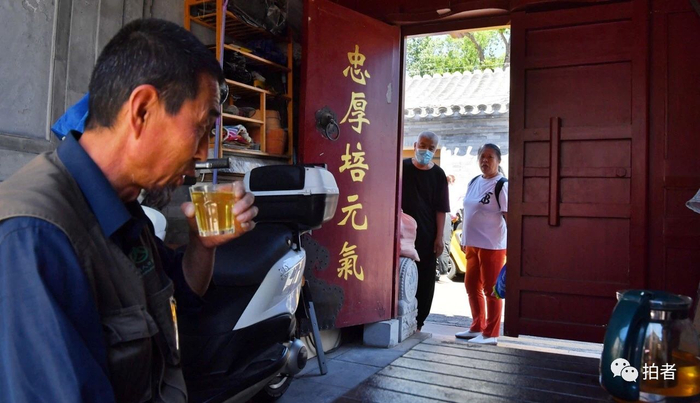 邹立明坐在门洞里边喝茶边和邻居聊天。