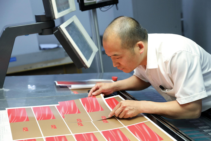 技术人员认真审看刚刚打印完成的请柬版样，努力做到颜色与模板分毫不差，为下一步印制图案和字体做好准备。