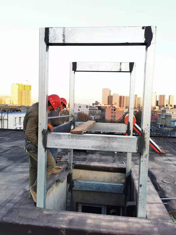 工人在楼顶的天井口焊接组装电梯钢结构井道。