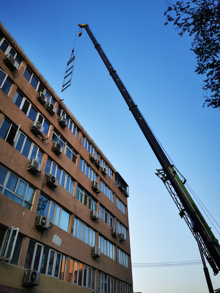 施工人员用吊车将钢结构井道吊上楼顶。