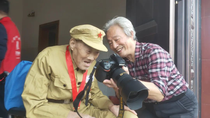 摄影师何荣发向志愿军老兵周荣富展示拍好的照片。薛余华摄