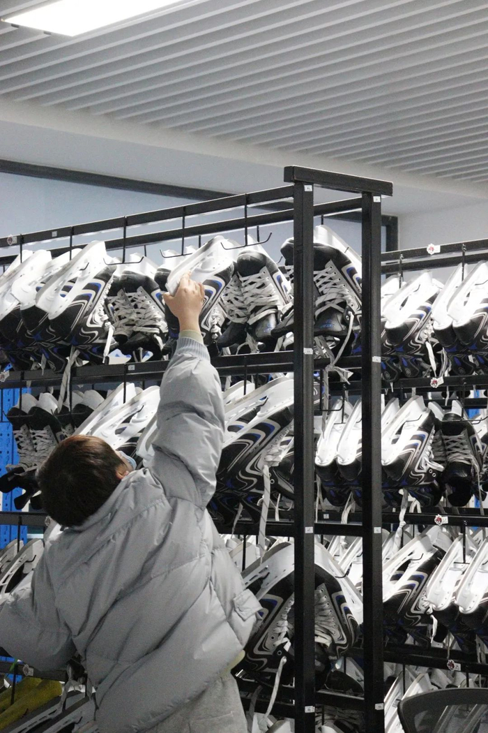 冰鞋被整整齐齐地挂在架子上，工作人员正在取鞋。