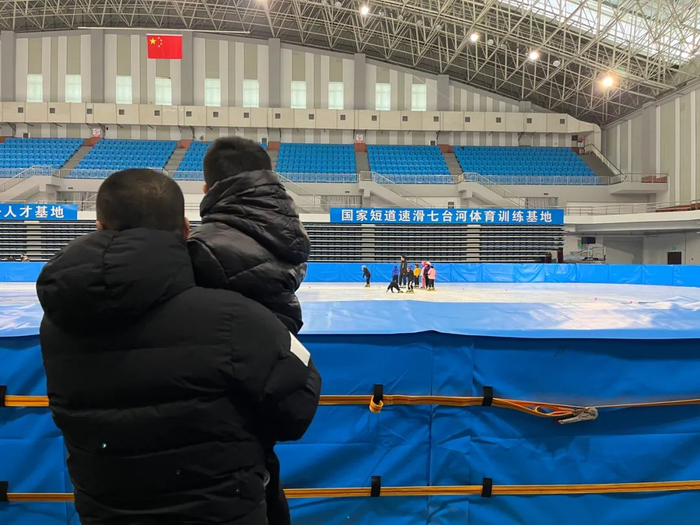 　　2022年2月14日，七台河体育中心室内冰场。有孩子想来学滑冰，家长抱着他观看训练。新京报记者 杜寒三 摄