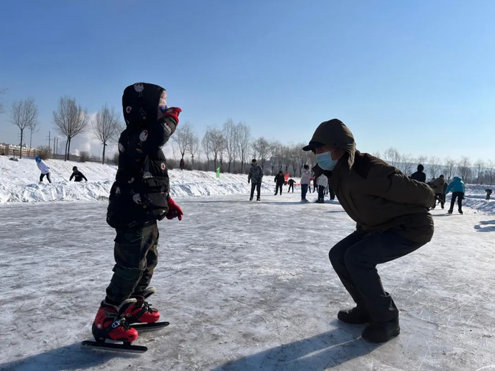 2022年2月13日，万宝荷花池野冰场，一位大爷在给7岁的孙女示范动作。新京报记者 杜寒三 摄