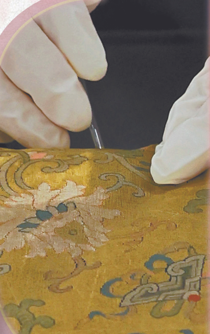 使用真空高压液态过滤吸尘器给清道光黄色缂丝勾莲庆纹方凳垫除尘。