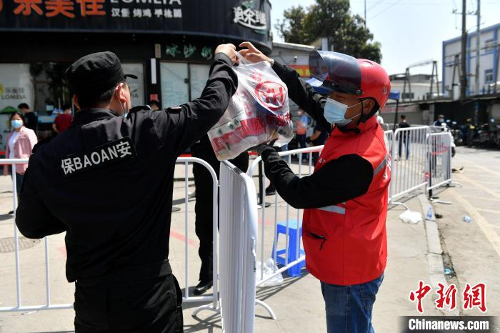图为外卖小哥将生活物资交给管控区的安保人员。　吕明 摄